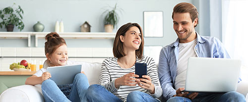 Daughter, mother and father sitting on couch looking at electronic devices