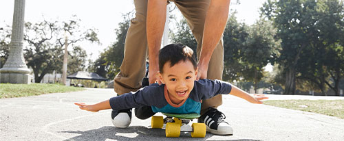 small boy on a skateboard being helped to stay steady by an adult