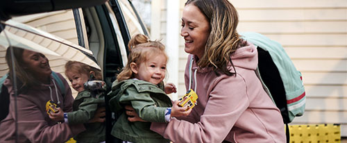 mom getting little girl out of car and both smiling