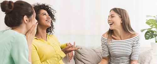 Three women sitting on a couch, smiling, laughing and talking